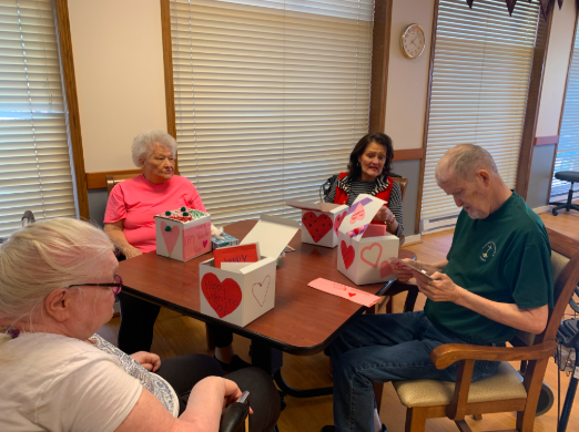 Distribution Day: Gathered around a table, four elders from the Gretna Family Community Center are reading their Valentine Day cards. The cards were made throughout the week of Feb. 13 and were created by a combination of students from grades K-12. Each elder received about five cards in their boxes.