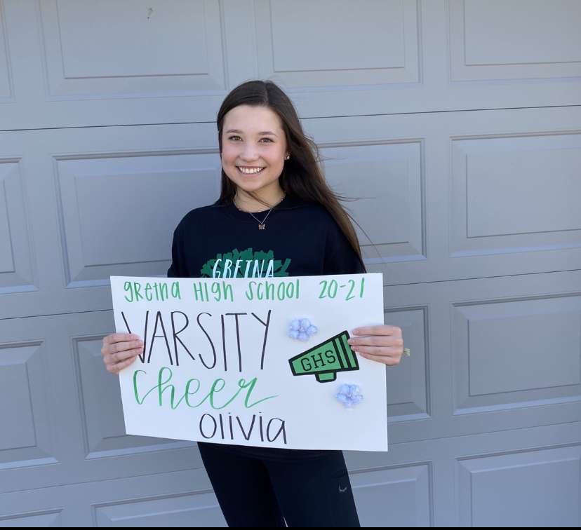After making the varsity cheer team, sophomore Oliva Runge holds up a sign she received from her coach. Every member of the varsity cheer team got the same sign with their own name on it, along with a team shirt. This will be Runges third year on the team.
