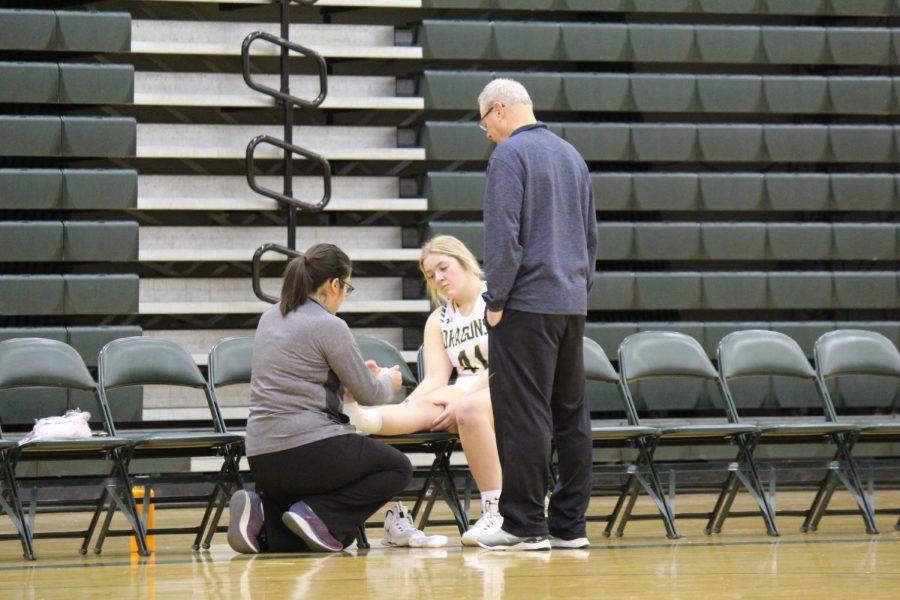 Out for now. Coach Jerone Skrdla and  team trainer Katia Lira Garcia examine Addi Armitage (25) after her injury in the Omaha Central game on January 27 2022. They determined that she would not continue to play in that game.