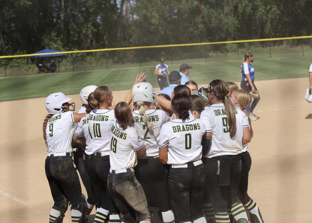 The varsity softball team gathers into a huddle to cheer on a teammate as she stomps on home plate. 
