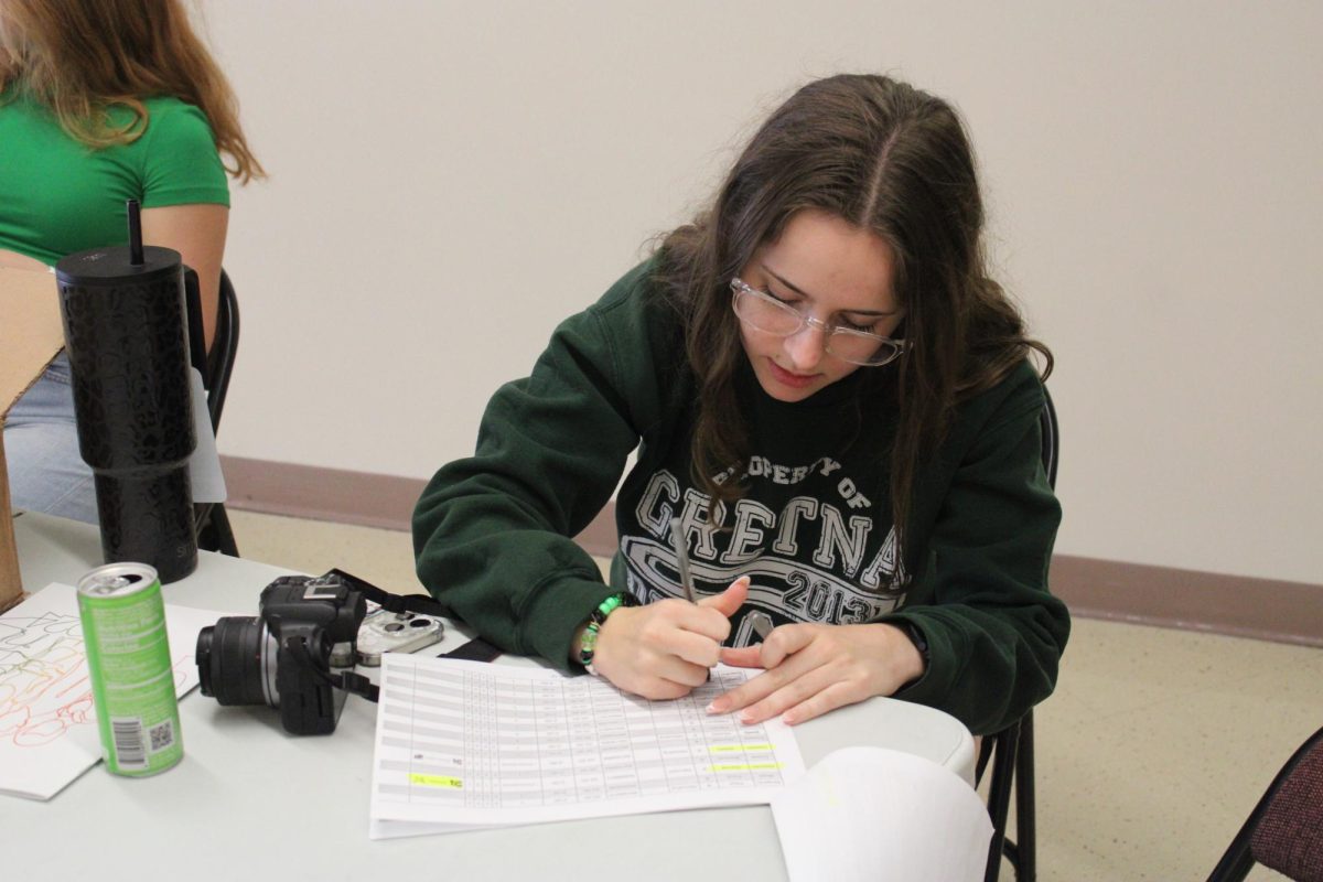 Yearbook editor in chief Kierstin Gay (25) crosses off names from a list as she hands out middle school yearbooks to incoming freshmen at Freshmen Day on Tuesday, Aug. 13.