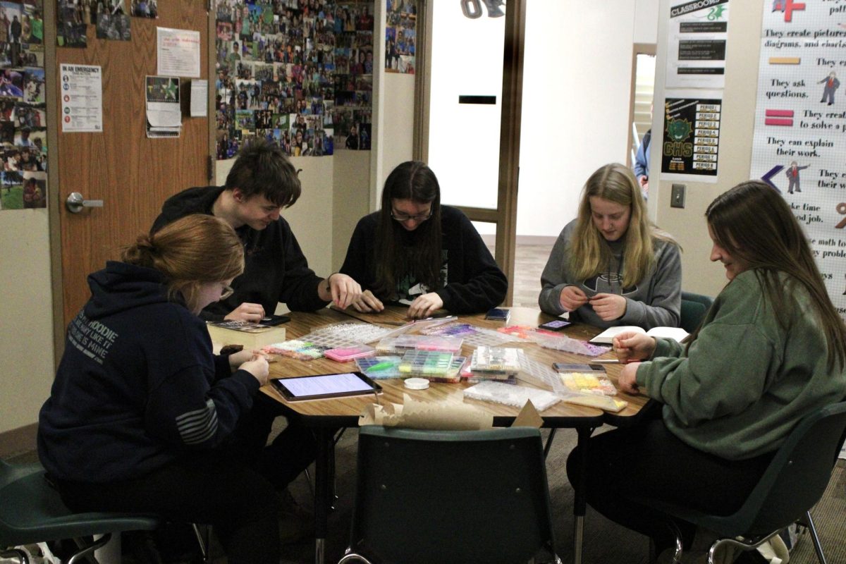 Sophomores Cassidy Lacy, Kaden Bauer, Kirsten VonSeggern, Lillian Bock and Kerrington Dillman sit around a table in Neil Hammond's room on Jan. 28, making bracelets with Bible verses or other charms.