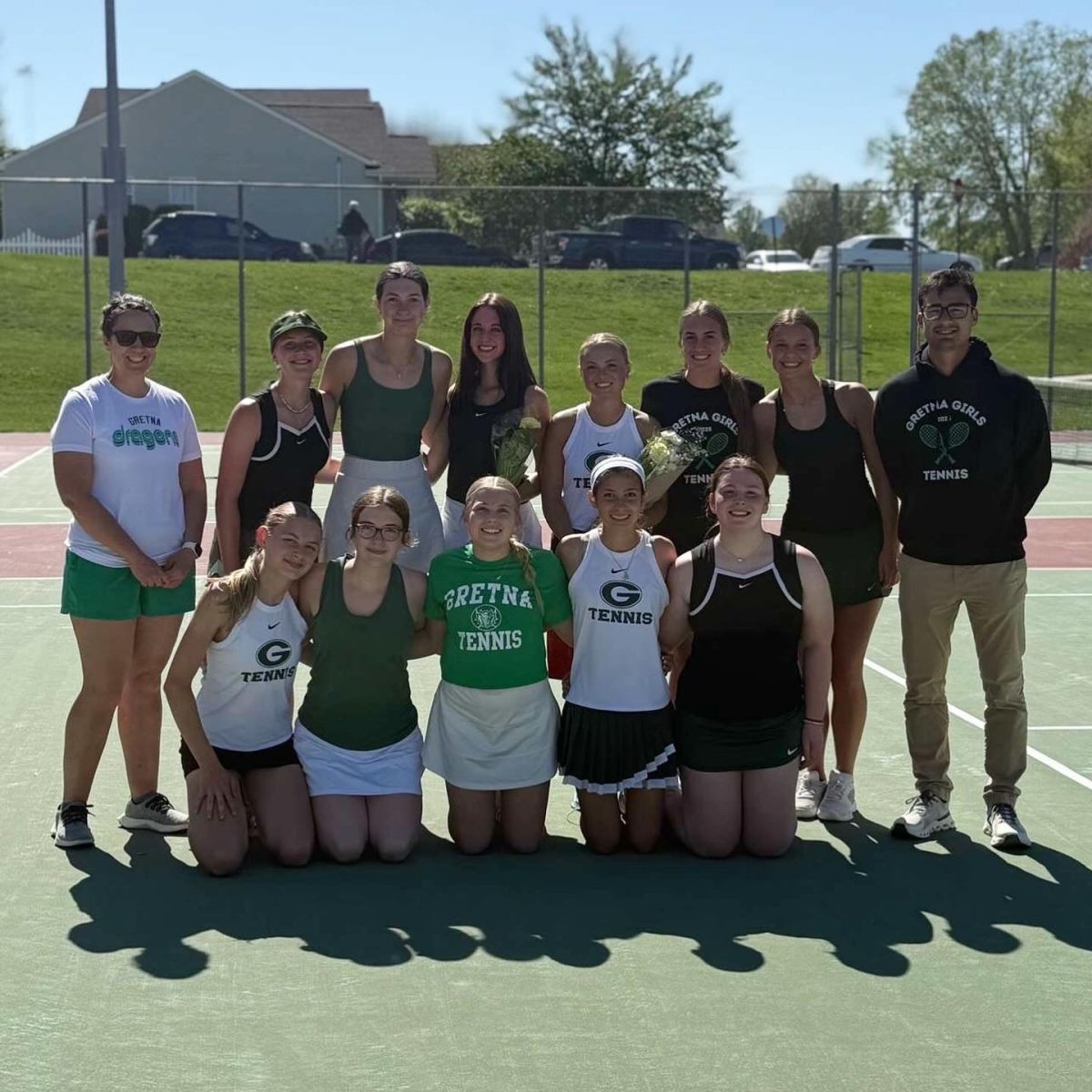 Both seniors Abbie Zavadil and Mia Yungtum pose for a picture with the girls' tennis team on senior nights with coaches Sarah Benzel and Noah Bernal.